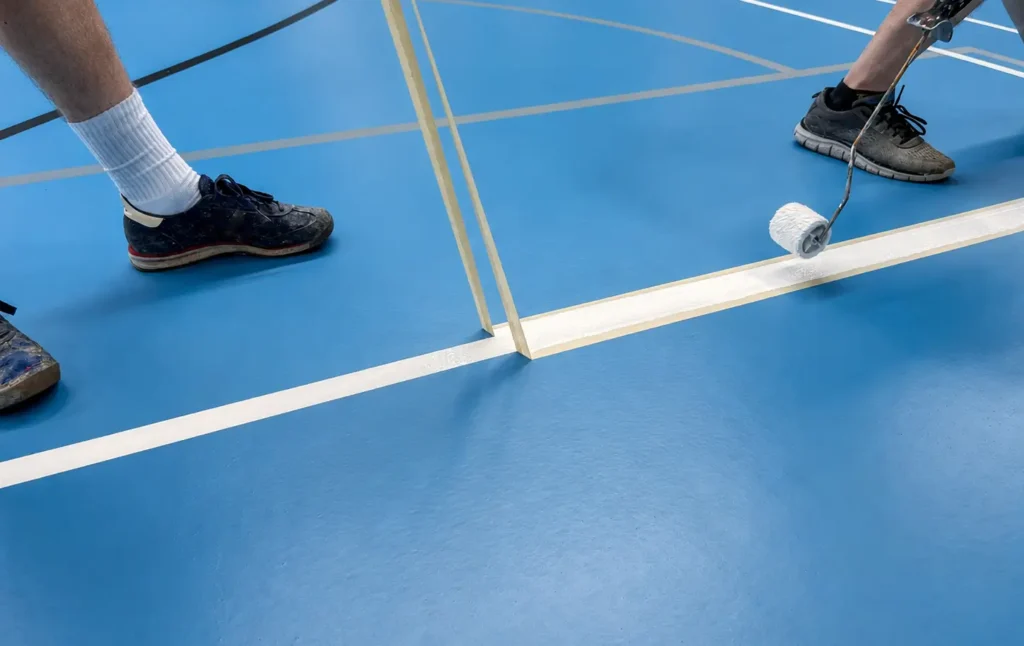 Udførere arbejder med præcis opmåling og baneopstregning på et nyt blåt sportsgulv