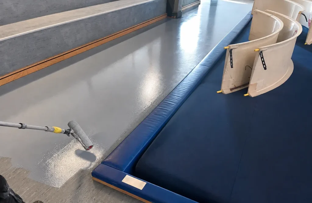 Udfører påfører en ny blå overflade på sportsgulvet med rulle
