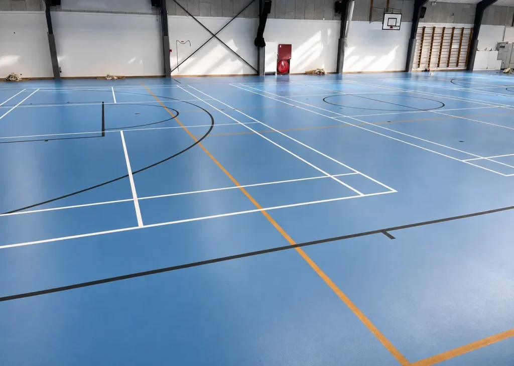 Renoveret sportshal med blå gulvoverflade og røde, orange, hvide og sorte banelinjer